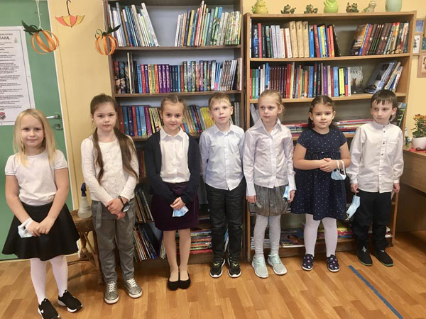 Uczniowie w bibliotece. Dzieci stoją, za nimi regały z książkami.