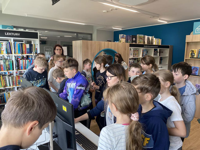 Biblioteka - regały z książkami, grupa dzieci.