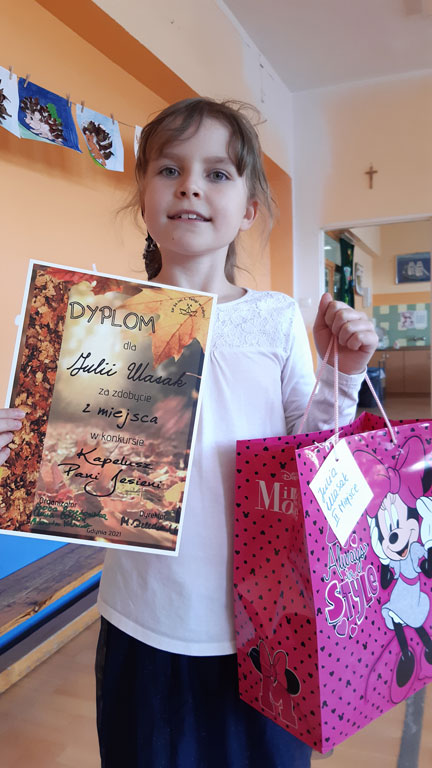 Dziewczynka trzyma dyplom i kolorową torbę z prezentami.