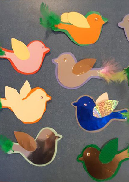 Prace Świetliczaków - kolorowe ptaszki z papieru ozdobione piórkami.