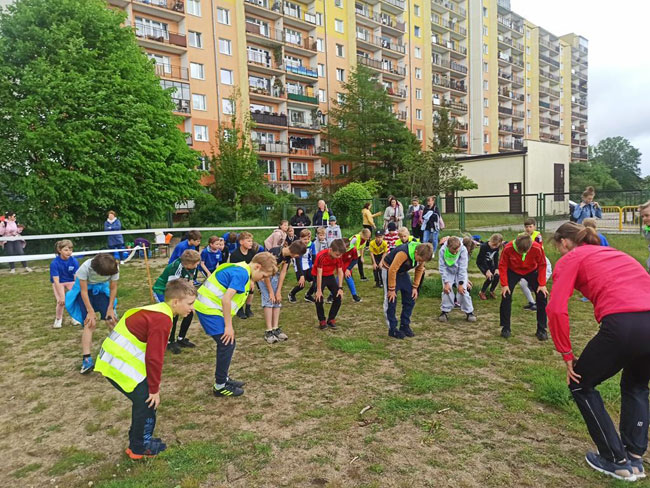 Boisko szkolne - gruoa dzieci rozgrzewających się przed biegiem.