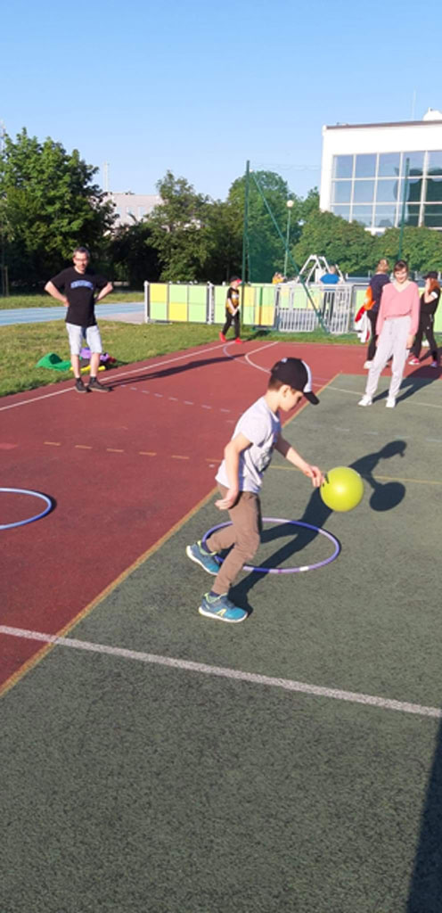Boisko szkolne - chłopiec kozłujący piłkę.