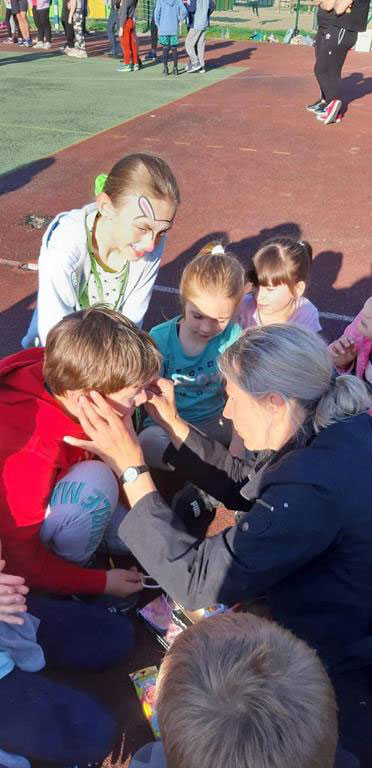 Grupa dzieci, kobieta maluje buzię chłopca.